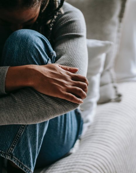 crop pitiful black woman embracing knees on bed